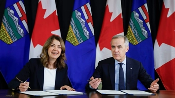 Two people at signing ceremony with Alberta and Canada flags backdrop
