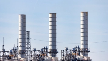 Three tall exhaust stacks and transmission towers at a power generation facility