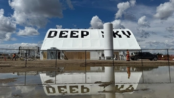 Large white inflated Deep Sky structure at an outdoor industrial site reflected in a puddle in the foreground