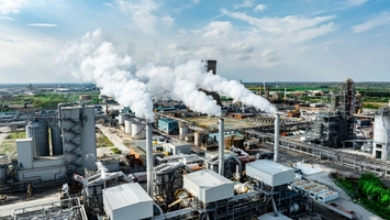 Aerial view of a large industrial complex with multiple smokestacks releasing white steam against a blue sky