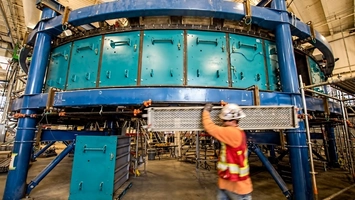 Construction worker in hi-vis gear lifting scaffolding beside a large circular industrial carbon capture unit