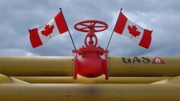 Red industrial pipeline valve with two Canadian flags mounted on yellow gas pipework under a cloudy sky